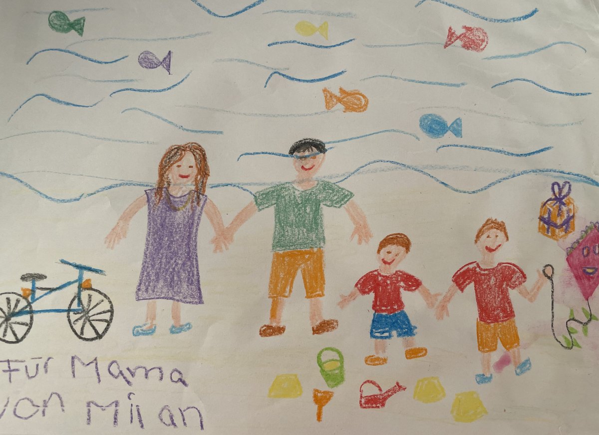 Kinderzeichnung: Familie Hand in Hand am Strand, mit Fischen, Fahrrad und Drachen; in der Ecke steht handschriftlich &bdquo;Für Mama von Milan&ldquo;